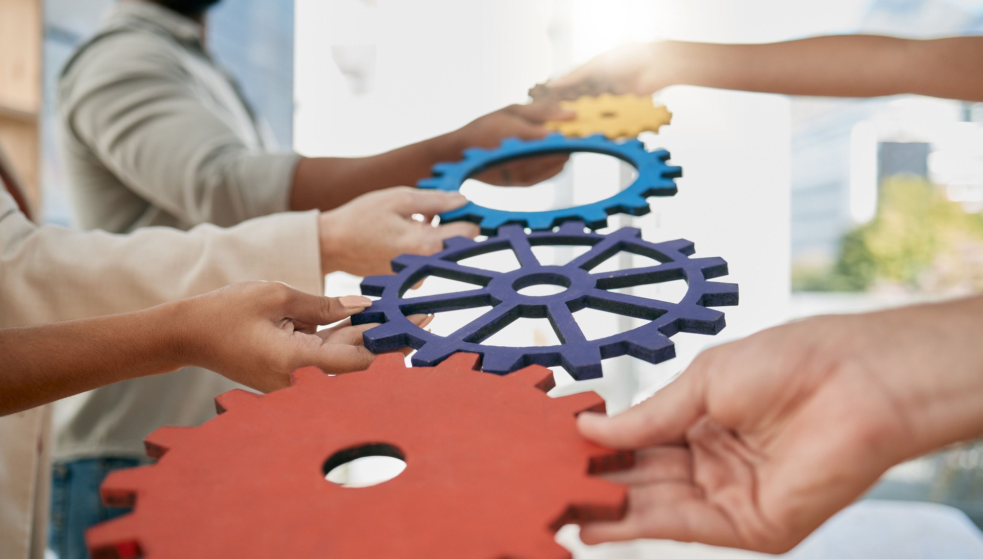Business people, toys and gears at job for teamwork, sign or symbol with solution, trust and solidarity. Corporate group, learning or development at team building exercise in city workplace for goals